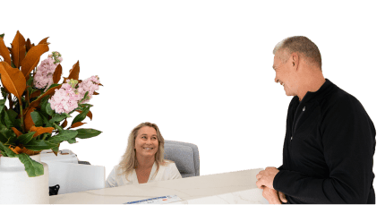 Receptionist at Mulgrave Dental Group warmly greeting a smiling patient at the front desk, with fresh flowers in the foreground.
