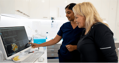 Dr. Diluni in a consultation with a Mulgrave Dental Group patient, pointing at a computer screen showing 3D models.