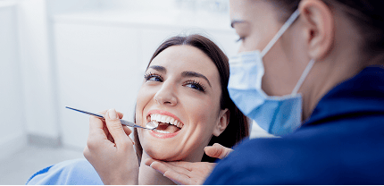 Smiling patient receiving a professional dental scale and clean, with a dentist using a mouth mirror during the check-up.