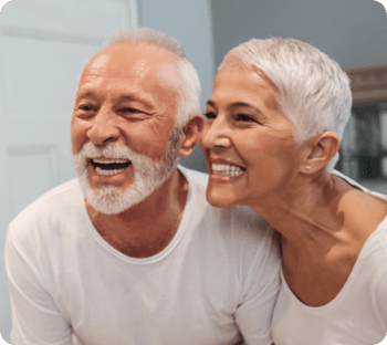 An older couple looking at the mirror smiling and admiring their dental implants.