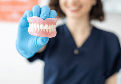 Close-up of a dental professional holding a set of natural-looking dentures, highlighting their realistic appearance and craftsmanship.
