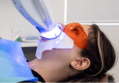 A Mulgrave Dental Group patient undergoing Zoom teeth whitening. She is wearing protective goggles while a specialised whitening machine shines light on her teeth.