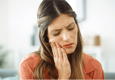 Woman holding her cheek in pain, showing signs of a dental emergency such as toothache or jaw discomfort.