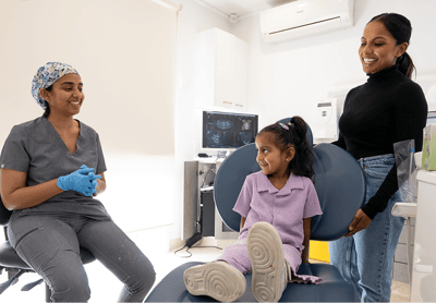Dr. Diluni chatting with a smiling child and parent during a friendly dental visit in a bright, modern clinic.