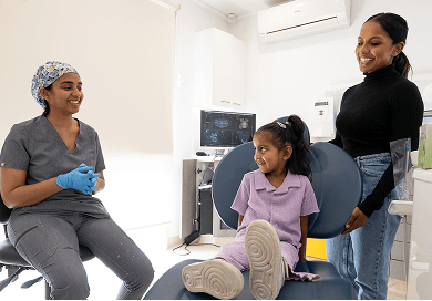 Dr. Diluni chatting with a smiling child and parent during a friendly dental visit in a bright, modern clinic.