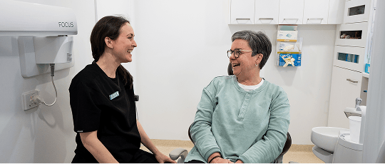 An Oral Health Therapist at Mulgrave Dental Group smiles warmly while interacting with a patient. Both appear relaxed and engaged, reflecting a friendly and caring dental experience.