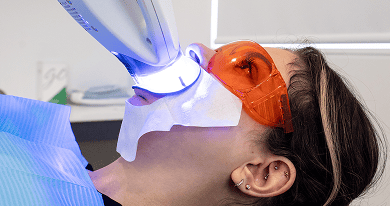 A Mulgrave Dental Group patient undergoing Zoom teeth whitening. She is wearing protective goggles while a specialised whitening machine shines light on her teeth.