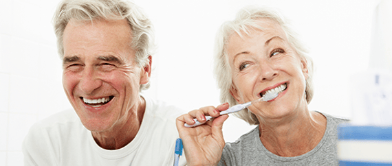 Smiling older couple brushing their teeth together at home.