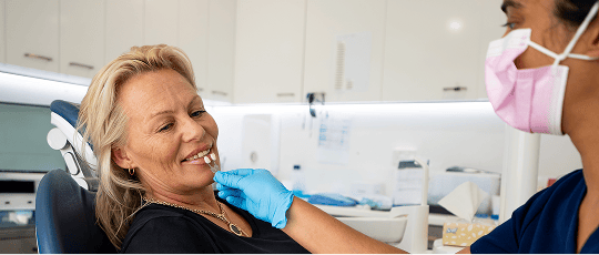Mulgrave Dental Group dentist and patient in a dental bridge consultation, with Dr. Diluni holding teeth colour samples to compare the shade with the patient's natural teeth.