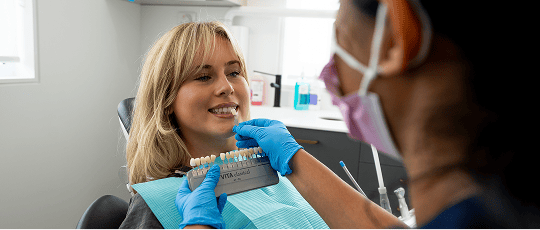 Dr. Diluni holding a tooth colour sample, carefully comparing it to a Mulgrave Dental Group patient's natural tooth shade during the dental crown fitting process.