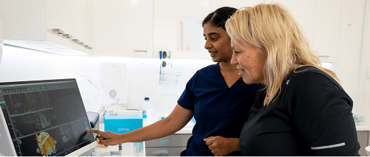 Dr. Diluni in a consultation with a Mulgrave Dental Group patient, pointing at a computer screen showing 3D models.