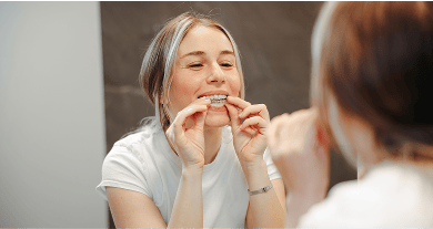 A woman at home, using a take-home teeth whitening kit and putting the custom tray with whitening gel onto her teeth.