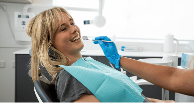 Mulgrave Dental Group patient smiling while seated in the dentist’s chair, as a dentist holds a mouth mirror during a check-up.