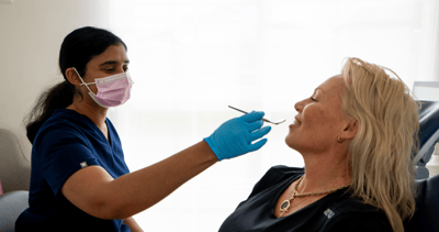 Dr. Diluni about to inspect a Mulgrave Dental Group patient's teeth with a mouth mirror.