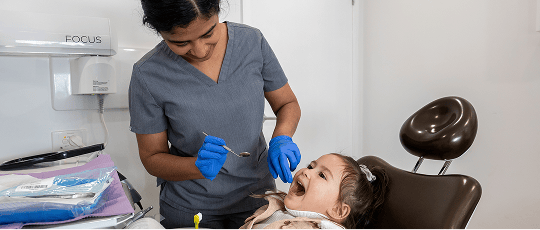 Dr. Diluni gently examining a young child's teeth with a mouth mirror.