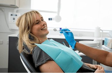 Mulgrave Dental Group patient smiling while seated in the dentist’s chair, as a dentist holds a mouth mirror during a check-up.