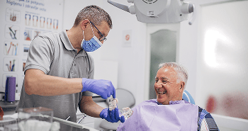 Dentist holding a dental model and showing a patient how dental implants work.