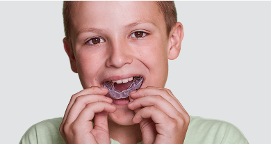 Young boy inserting a dental mouthguard into his mouth.