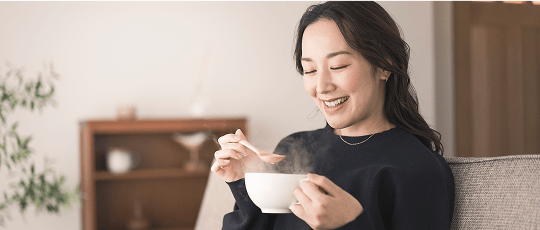 Smiling woman at home having a bowl of soup.