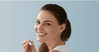 Smiling woman holding a clear aligner.