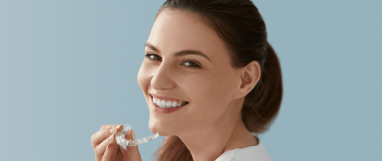 Smiling woman holding a clear aligner.