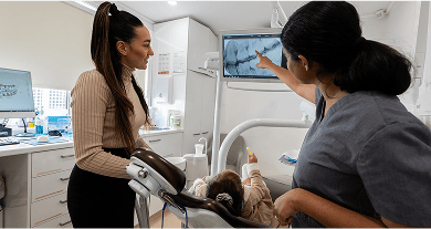 Dr. Diluni shows an X-ray and explains it to a parent while their child sits in the dental chair holding a new toothbrush.