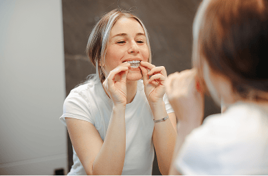 A woman at home, using a take-home teeth whitening kit and putting the custom tray with whitening gel onto her teeth.