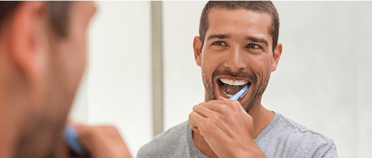 Man looking in the mirror while brushing his teeth at home.