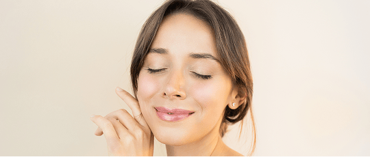 A smiling woman, gently touching her smooth, youthful skin.