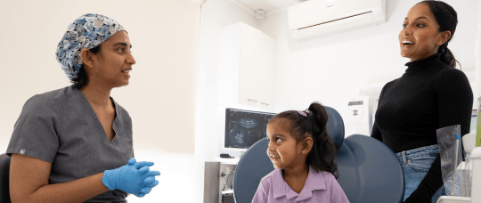 Dr. Diluni chatting with a smiling child and parent during a friendly dental visit in a bright, modern clinic.