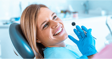Smiling woman in a dentist's chair with a dentist holding a mouth mirror.