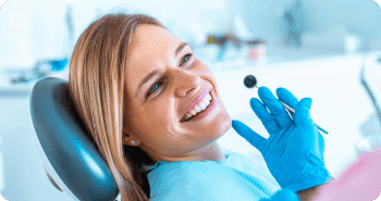 Smiling woman in the dentist's chair with the dentist's hand holding a mouth mirror during a dental check-up.