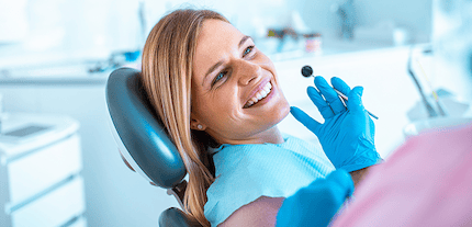 Smiling woman in a dentist's chair with a dentist holding a mouth mirror.