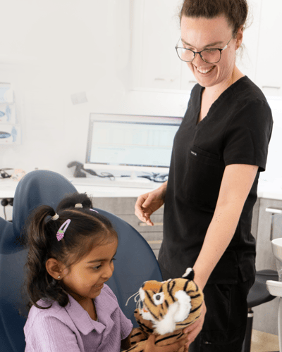 Image of a Mulgrave Dental Group staff member handing a cuddly stuffed animal toy to a happy child.