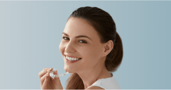 A woman smiling while holding her clear aligners.