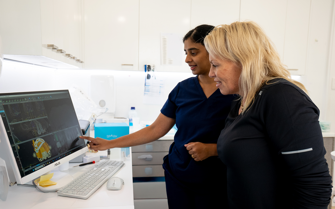 Dr. Diluni in a consultation with a Mulgrave Dental Group patient, pointing at a computer screen showing 3D models.